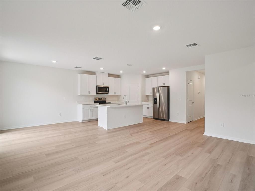 A bright kitchen with white cabinets, stainless steel appliances, and light wood-look flooring — 17661 OLIVE THORN DRIVE, BROOKSVILLE, FL
