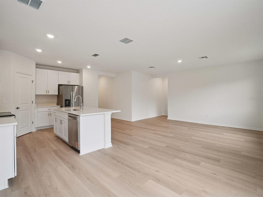 A modern kitchen with white cabinets and a center island opens into a spacious room — 17661 OLIVE THORN DRIVE, BROOKSVILLE, FL