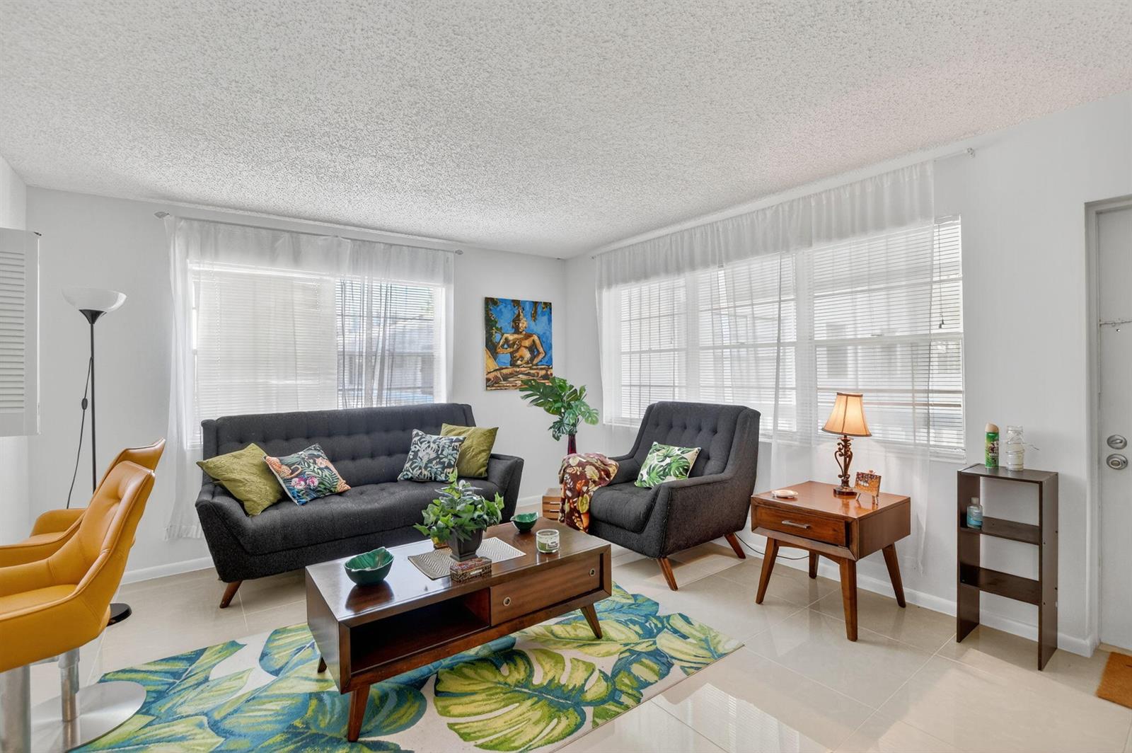 A living room features a dark sofa, armchair, mid-century coffee table, and a tropical area rug — 425 Durham N, Deerfield Beach FL 33442, DEERFIELD BEACH, FL