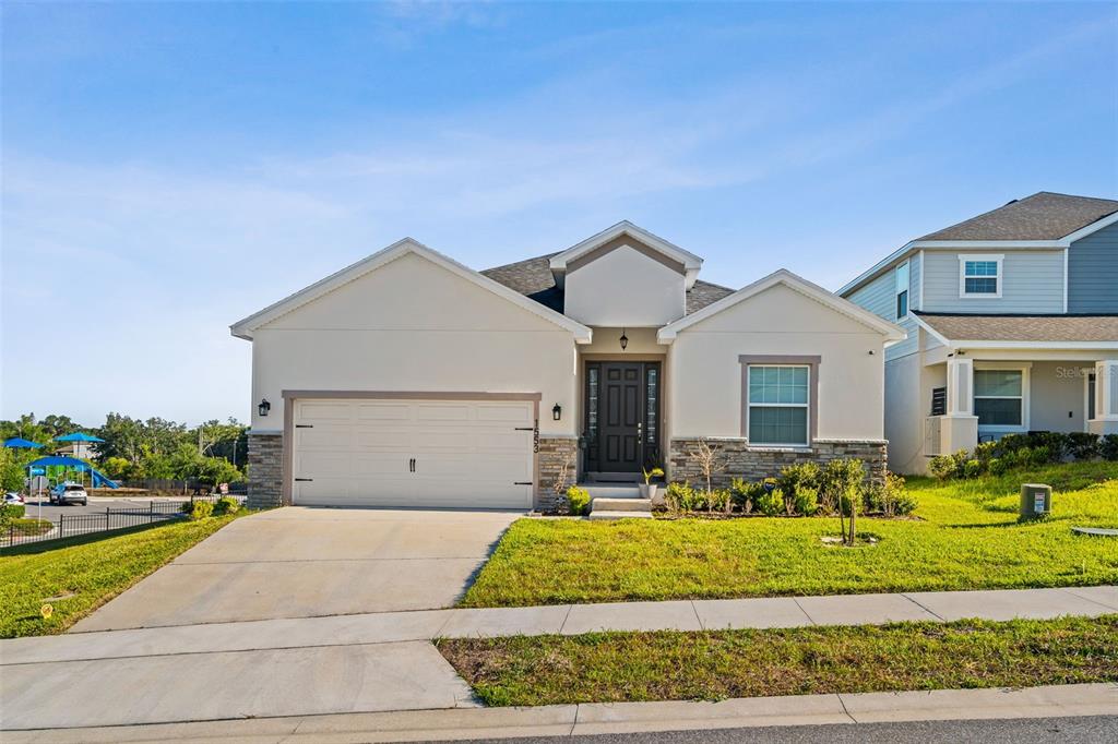 A single-story suburban house with a two-car garage, stone accents, and a grassy lawn — 1553 FLEUR DRIVE, DAVENPORT, FL