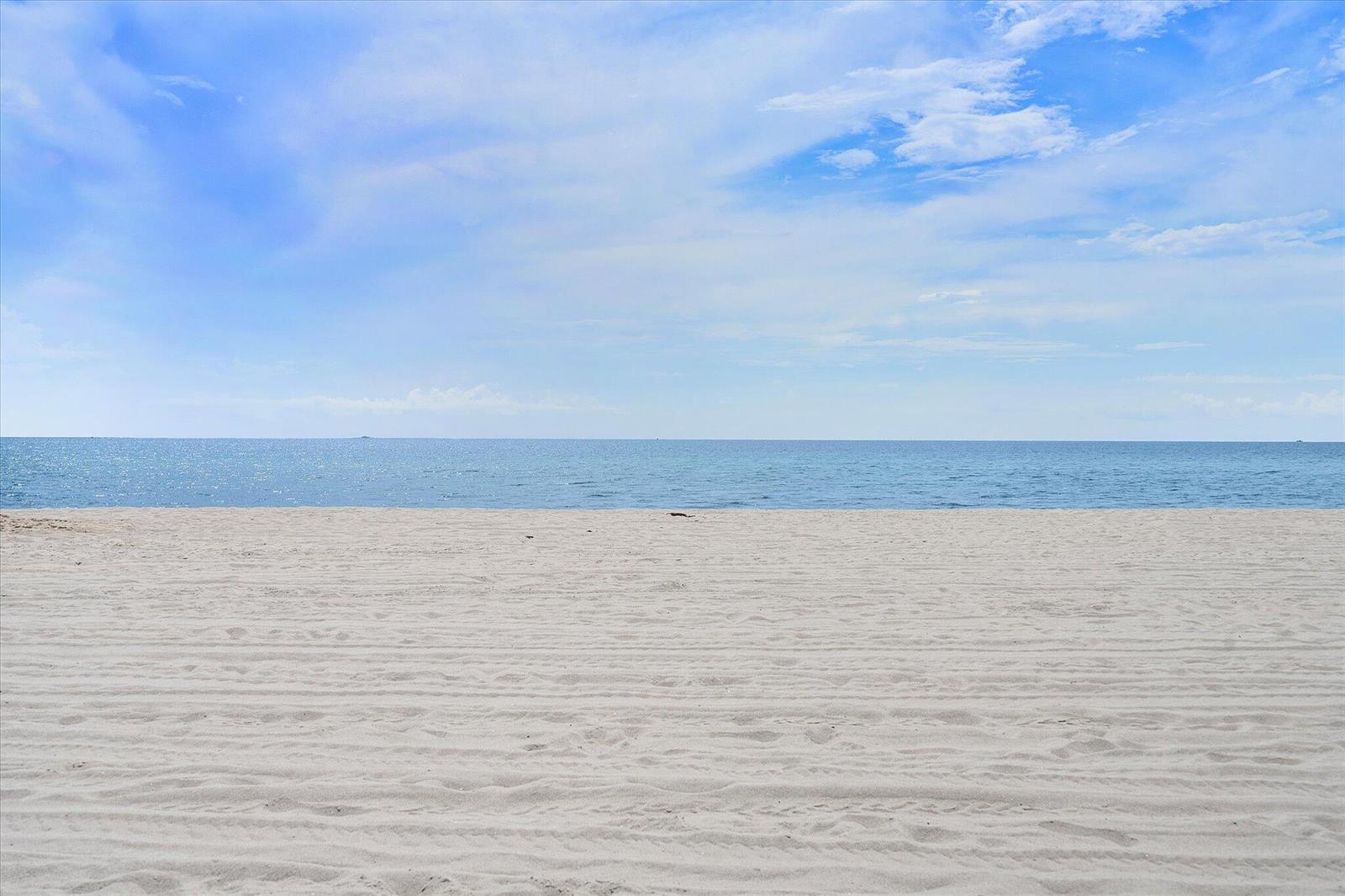A wide, sandy beach meets the calm blue ocean under a bright, partly cloudy sky — 1601 S Ocean Drive # 506, Hollywood FL 33019, HOLLYWOOD, FL