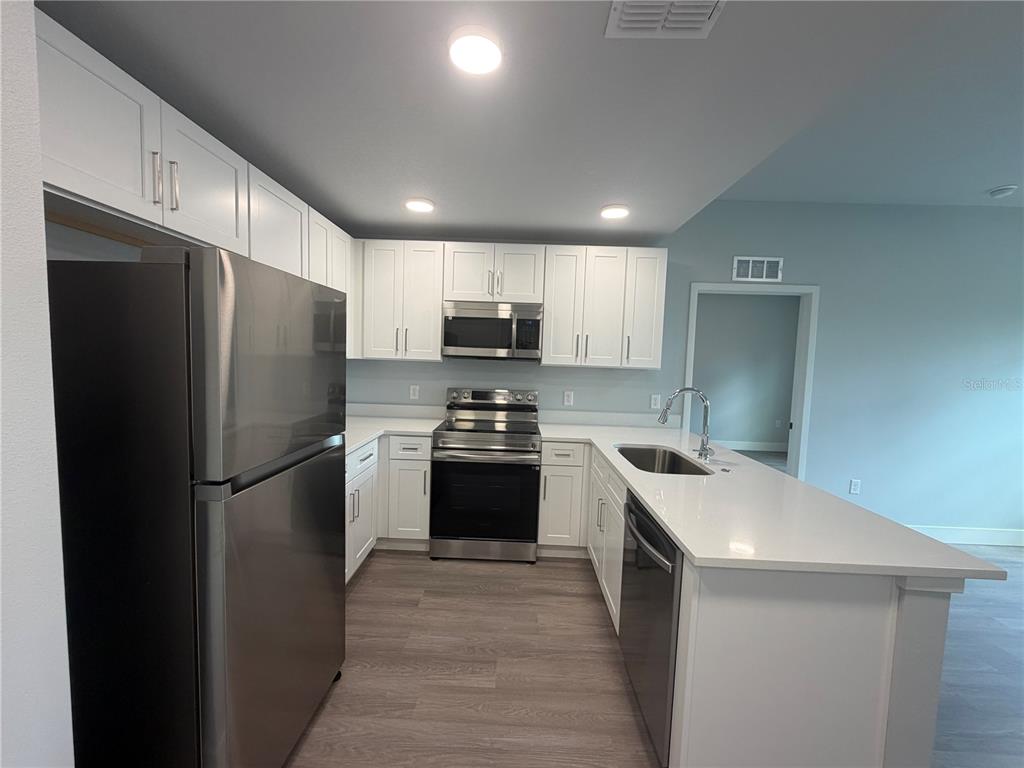 A kitchen features white cabinets, stainless steel appliances, and a quartz-topped island with a sink — 2240 FLORIDA DRIVE UNIT 203, DELTONA, FL
