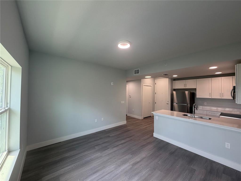 A living area with gray wood-look flooring opens to a kitchen with white cabinetry — 2240 FLORIDA DRIVE UNIT 203, DELTONA, FL