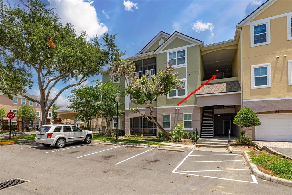 An exterior view of a multi-story apartment building with a parking lot and red arrow — 3315 PARKCHESTER SQUARE BOULEVARD UNIT 304, ORLANDO, FL