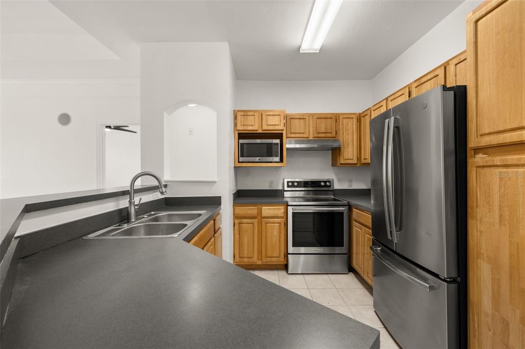 A kitchen features wood cabinets, stainless steel appliances, and dark countertops with a breakfast bar — 3315 PARKCHESTER SQUARE BOULEVARD UNIT 304, ORLANDO, FL