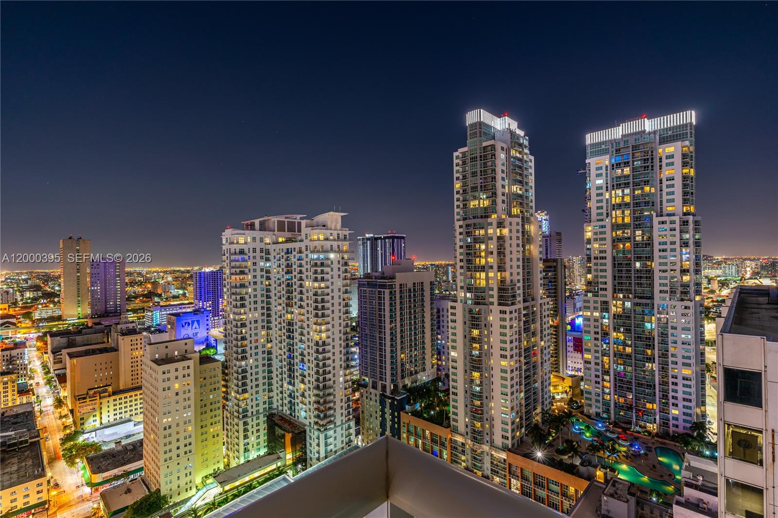 An elevated night view of a dense city skyline featuring several illuminated high-rise residential towers — 50 Biscayne Blvd # 3601, Miami FL 33132, MIAMI, FL