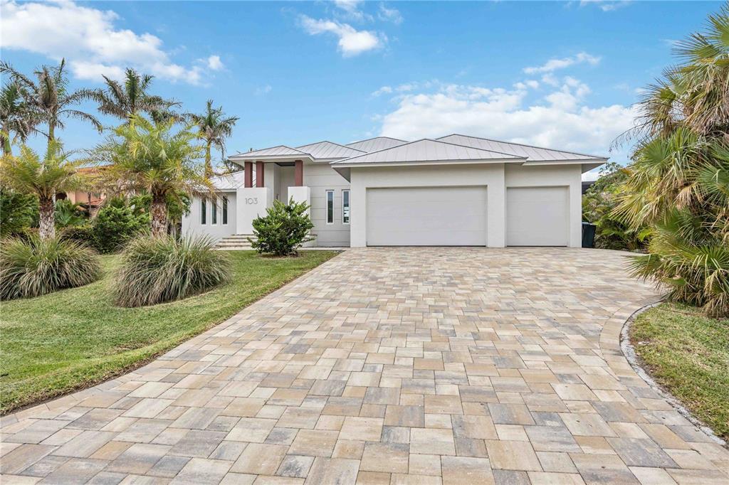 A modern single-story house features a paver driveway, a three-car garage, and palm trees — 103 GRAHAM STREET SE, PORT CHARLOTTE, FL