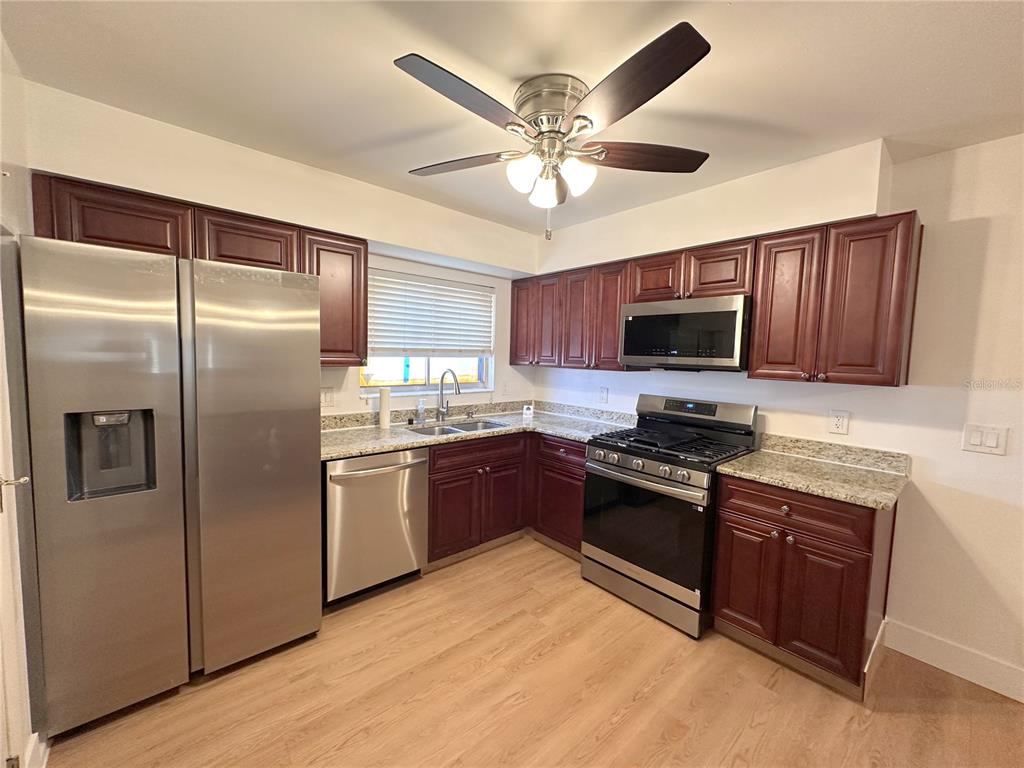 A kitchen features dark wood cabinets, stainless steel appliances, and light-colored granite countertops — 10848 WILDERNESS COURT, ORLANDO, FL