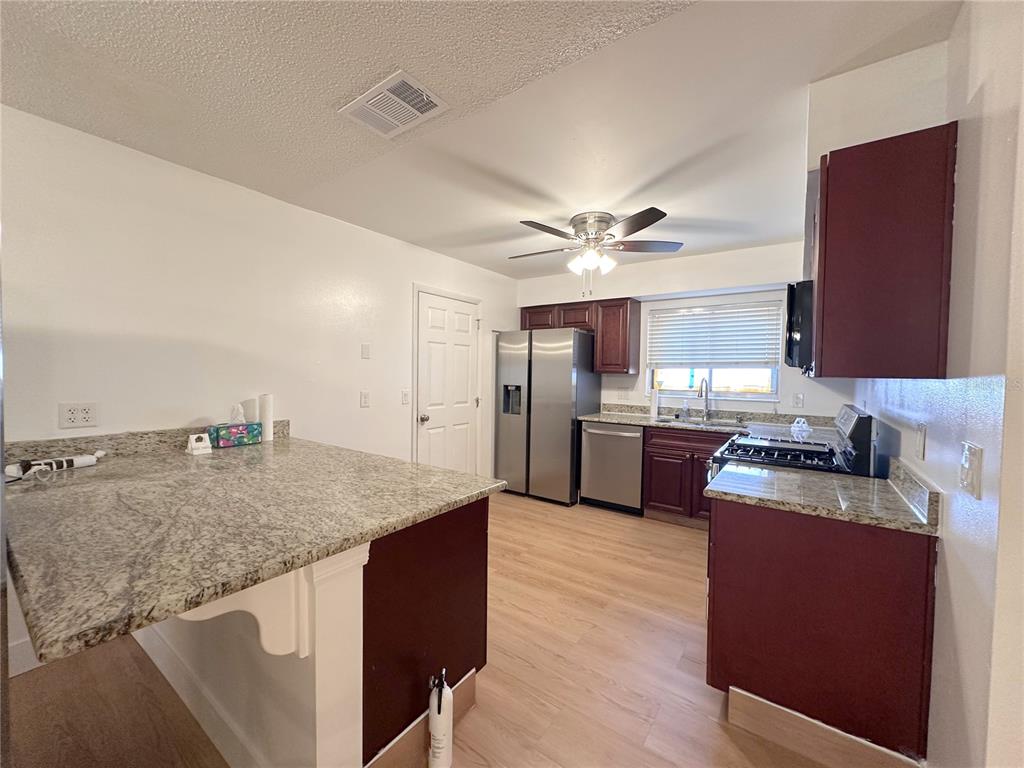 A kitchen features granite countertops, stainless steel appliances, dark wood cabinets, and light wood flooring — 10848 WILDERNESS COURT, ORLANDO, FL
