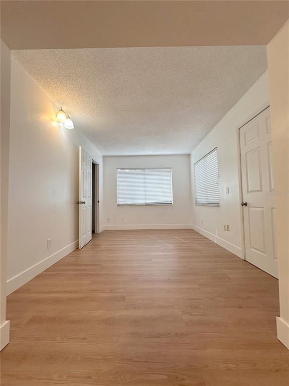 An empty room with light wood-look flooring, white walls, two windows, and two white doors — 10848 WILDERNESS COURT, ORLANDO, FL