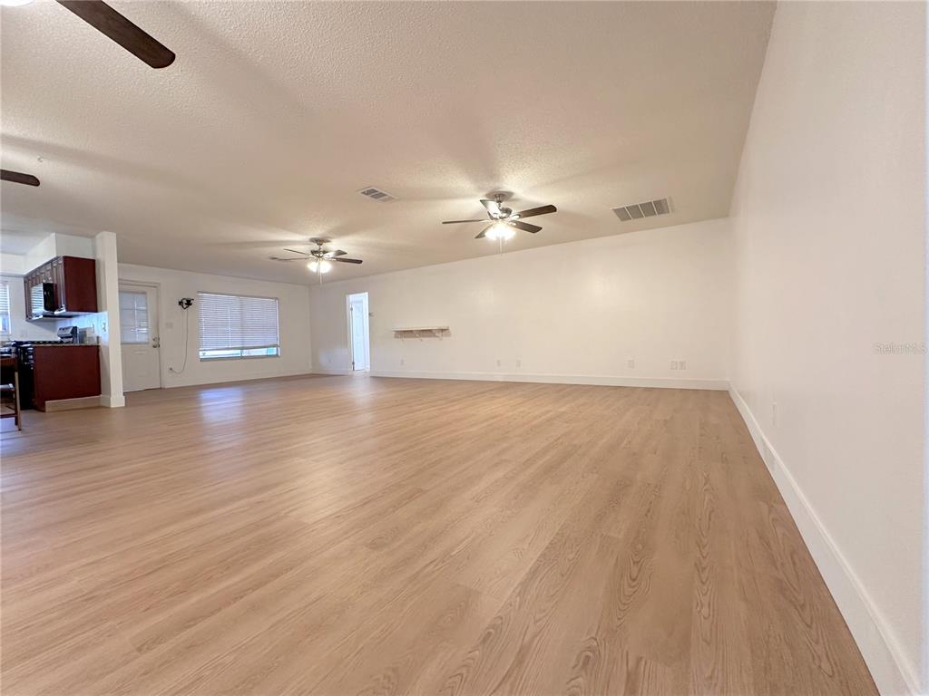 A spacious, open-concept living area features light wood-look flooring, white walls, and two ceiling fans — 10848 WILDERNESS COURT, ORLANDO, FL