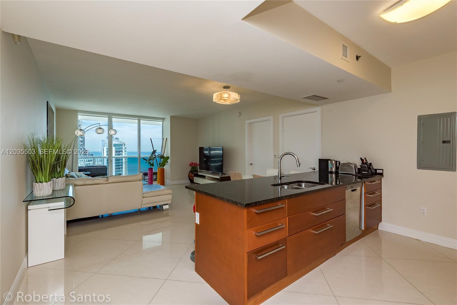 A modern kitchen island with dark countertops sits in an open-concept living area with ocean views — 1830 S Ocean Dr # 2410, Hallandale Beach FL 33009, HALLANDALE BEACH, FL
