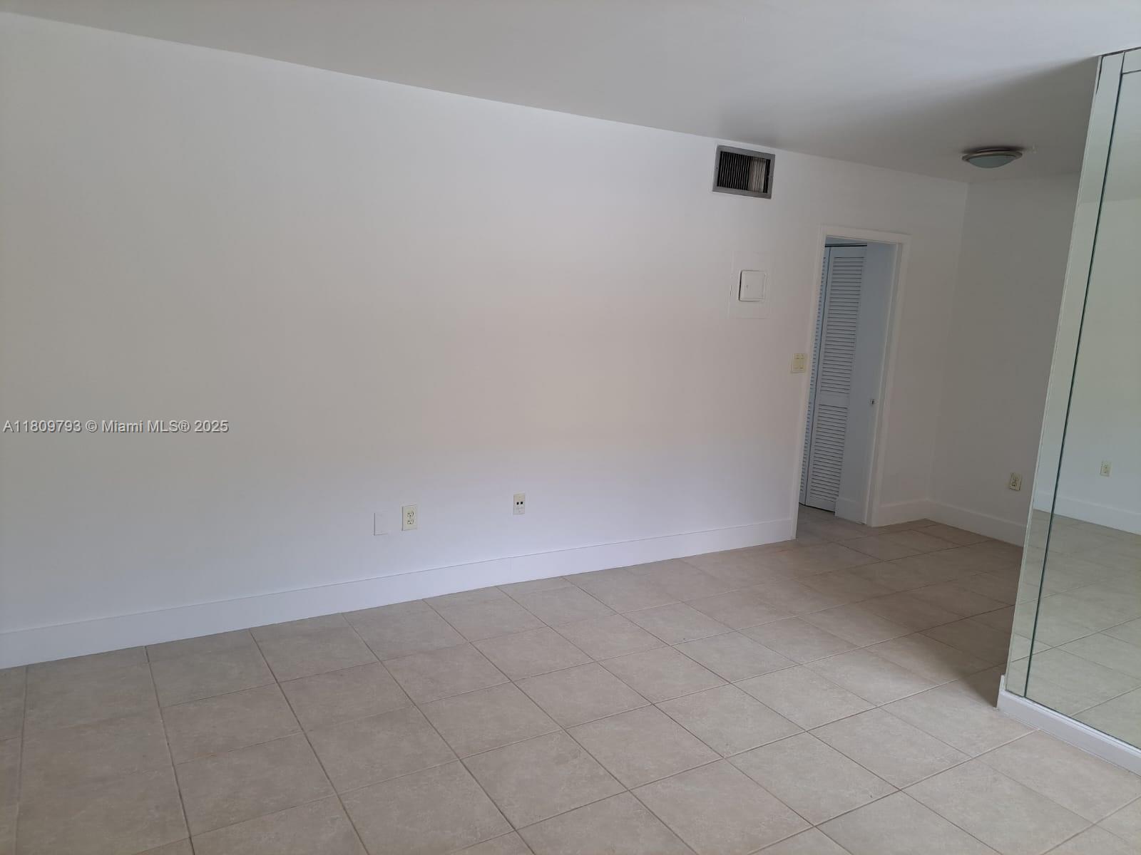 An empty room features white walls, beige tile flooring, and a mirrored closet door — 1975 NE 135th St # 2D, North Miami FL 33181, NORTH MIAMI, FL