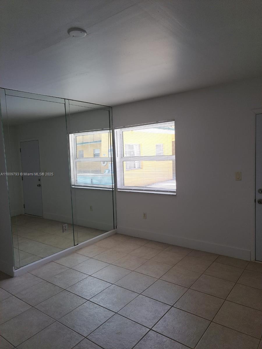 A room with tiled floors, mirrored closet doors, and two windows overlooking a yellow building — 1975 NE 135th St # 2D, North Miami FL 33181, NORTH MIAMI, FL