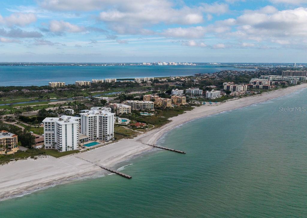 An aerial view shows beachfront high-rise condominiums along a sandy coastline with a calm ocean — 2295 GULF OF MEXICO DRIVE UNIT 54S, LONGBOAT KEY, FL