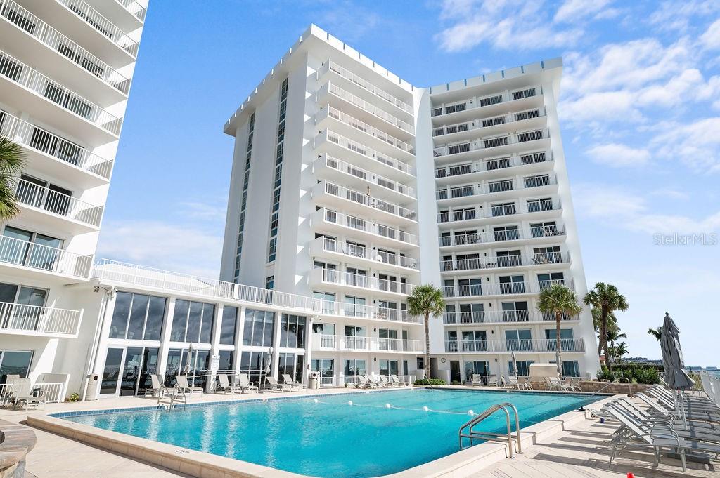 A swimming pool sits in front of a tall, white multi-story residential building — 2295 GULF OF MEXICO DRIVE UNIT 54S, LONGBOAT KEY, FL
