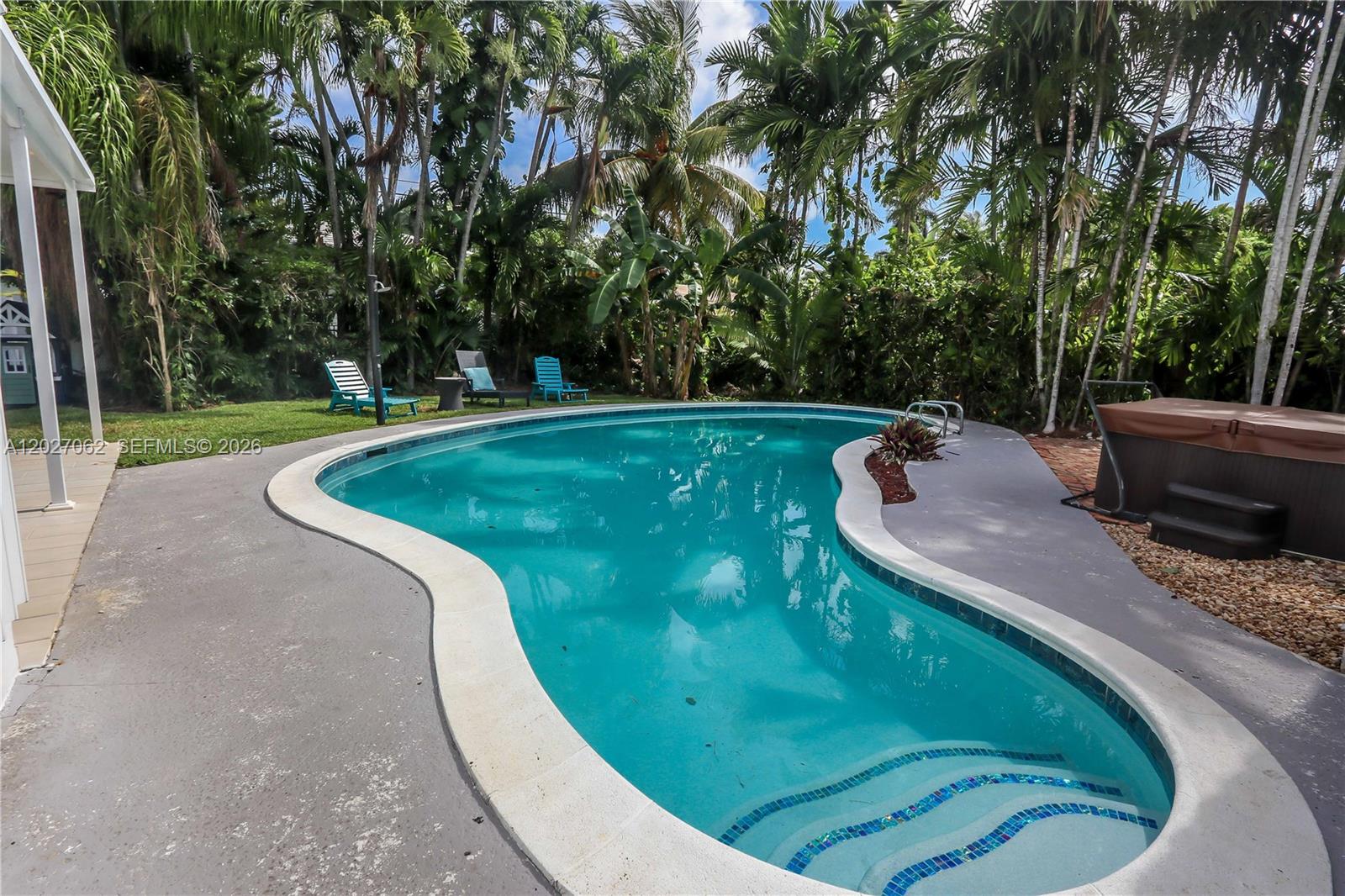 A kidney-shaped swimming pool sits in a backyard surrounded by lush tropical trees and landscaping — 955 Van Buren St, Hollywood FL 33019, HOLLYWOOD, FL