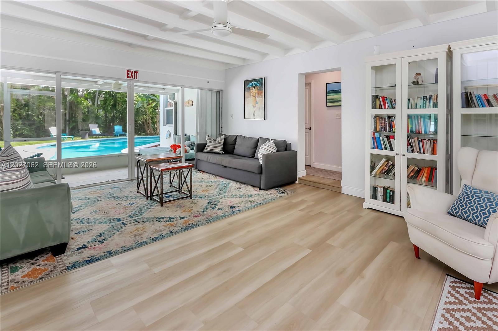 A living room features a gray sofa, white bookshelf, and sliding doors overlooking a swimming pool — 955 Van Buren St, Hollywood FL 33019, HOLLYWOOD, FL