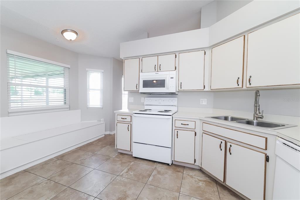 A kitchen with white cabinets, white appliances, tile flooring, and a built-in window bench — 177 TORTUGA COURT, DAVENPORT, FL
