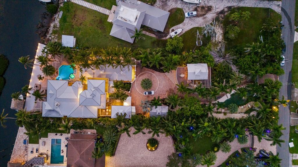 An aerial view shows a waterfront estate with a pool, circular driveway, and lush landscaping — 10216 46TH AVENUE W, BRADENTON, FL