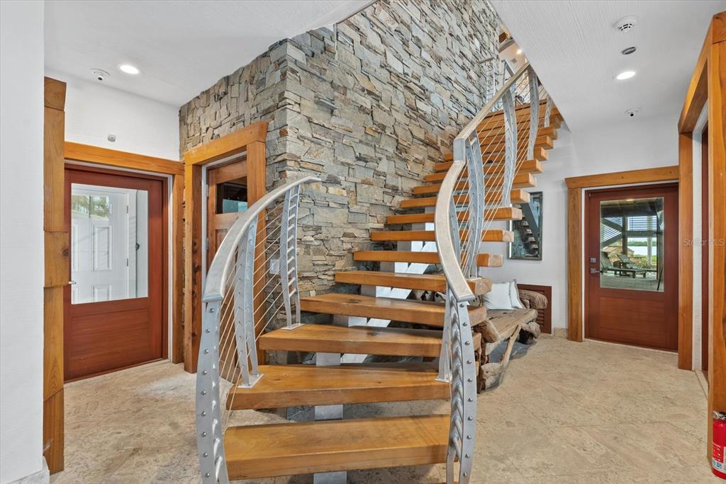 A foyer features a stone accent wall, a wooden floating staircase, and two wooden doors — 10216 46TH AVENUE W, BRADENTON, FL