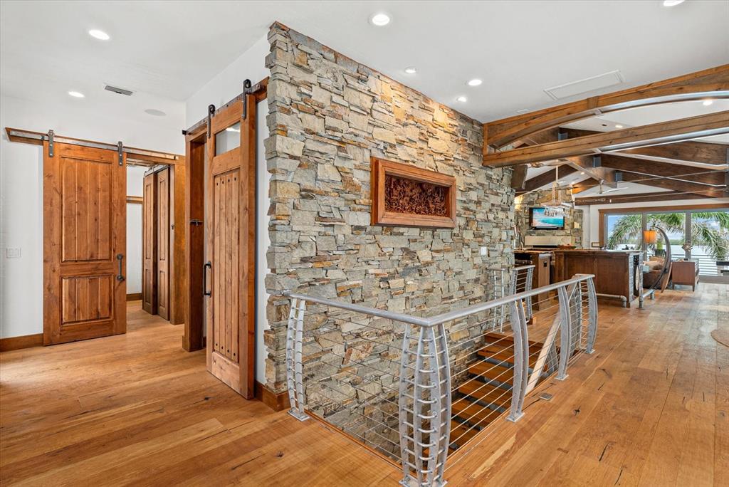 A stone wall separates a hallway with wooden barn doors from a staircase with railings — 10216 46TH AVENUE W, BRADENTON, FL