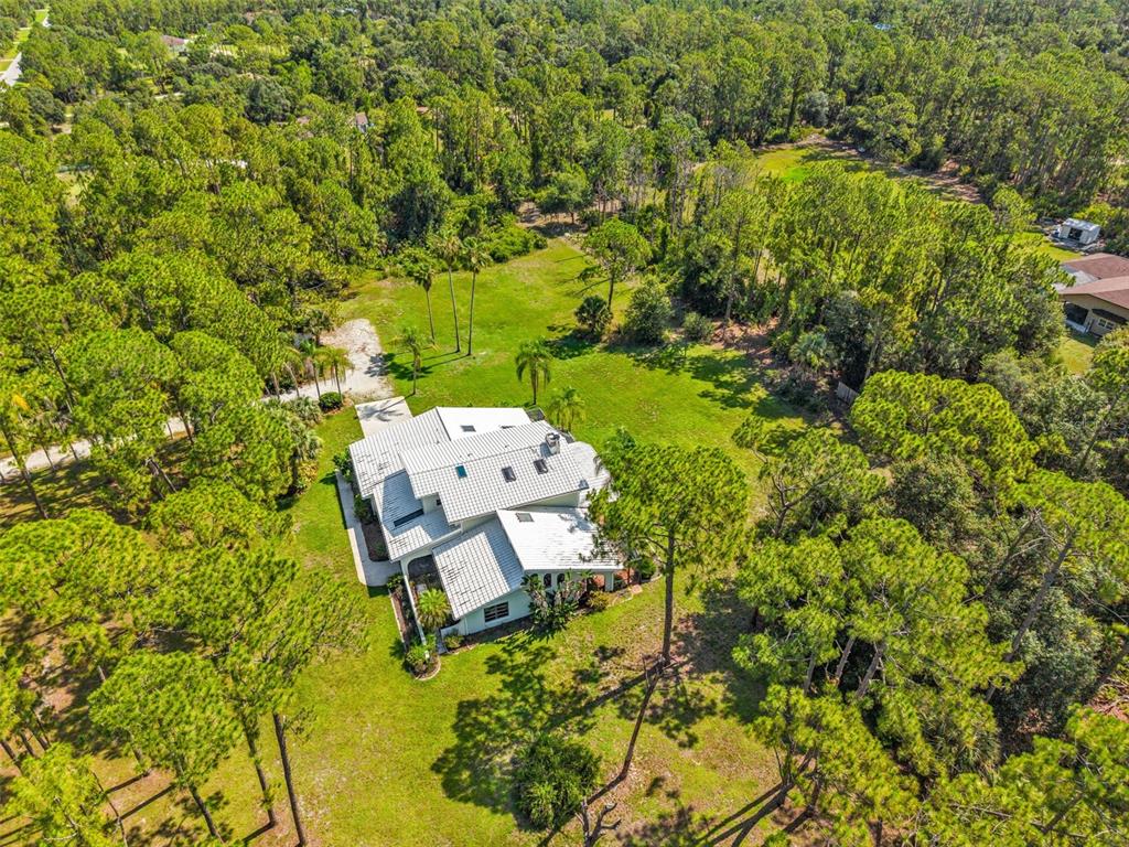 An aerial view shows a white house with a metal roof surrounded by pine trees — 6068 TIDWELL STREET, NORTH PORT, FL