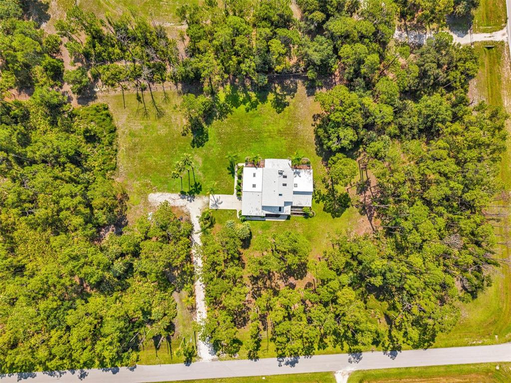 An aerial view shows a house with a white roof situated on a wooded lot — 6068 TIDWELL STREET, NORTH PORT, FL