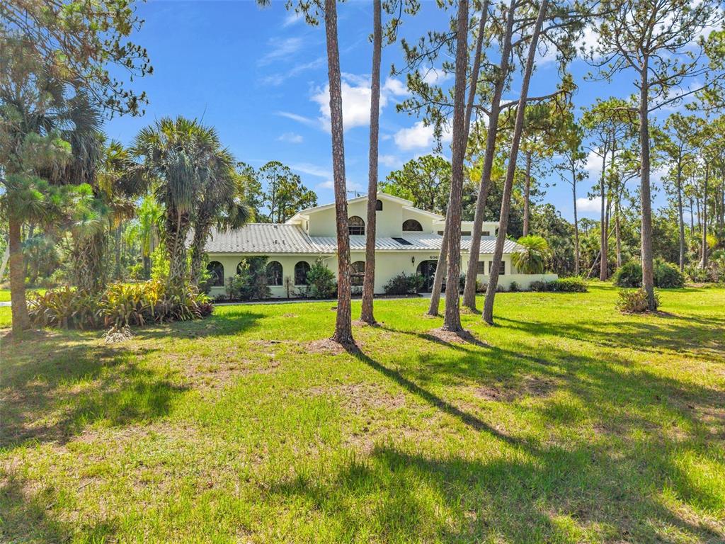 A light-colored house with arched windows sits on a grassy lot surrounded by pine trees — 6068 TIDWELL STREET, NORTH PORT, FL
