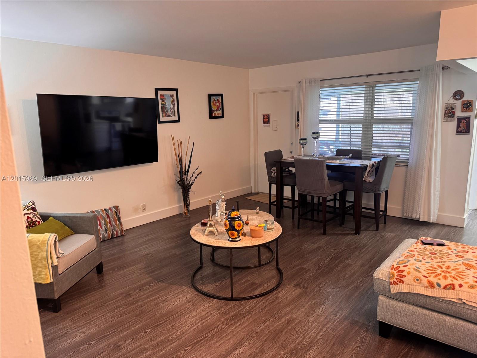 A living room with a wall-mounted television, a dining set, and dark wood-look flooring — 5300 Washington St # J214, Hollywood FL 33021, HOLLYWOOD, FL
