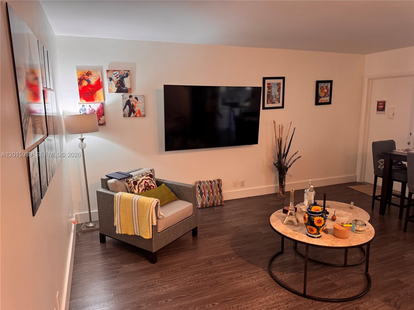 A living room features a wall-mounted television, a gray armchair, and a round coffee table — 5300 Washington St # J214, Hollywood FL 33021, HOLLYWOOD, FL