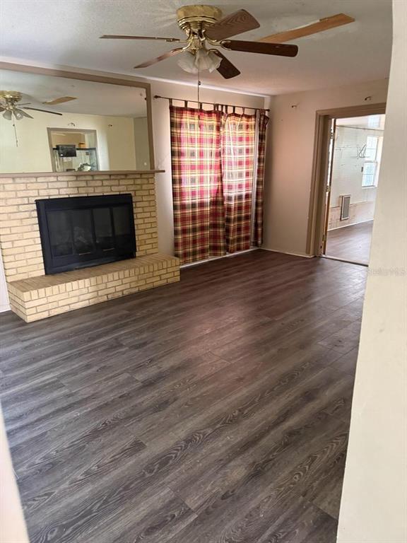 A living room features a brick fireplace, wood-look flooring, a ceiling fan, and plaid curtains — 3224 NW 30TH PLACE, GAINESVILLE, FL