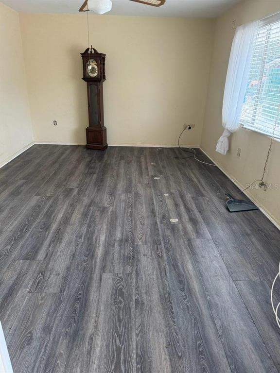 An empty room features dark wood-look laminate flooring, beige walls, and a tall grandfather clock — 3224 NW 30TH PLACE, GAINESVILLE, FL