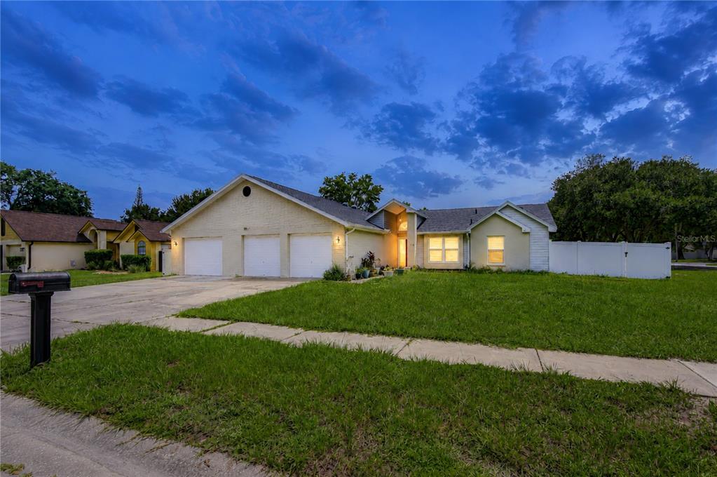 A single-story house with a three-car garage and a white fence at dusk — 1108 DOCKSIDE DRIVE, LUTZ, FL
