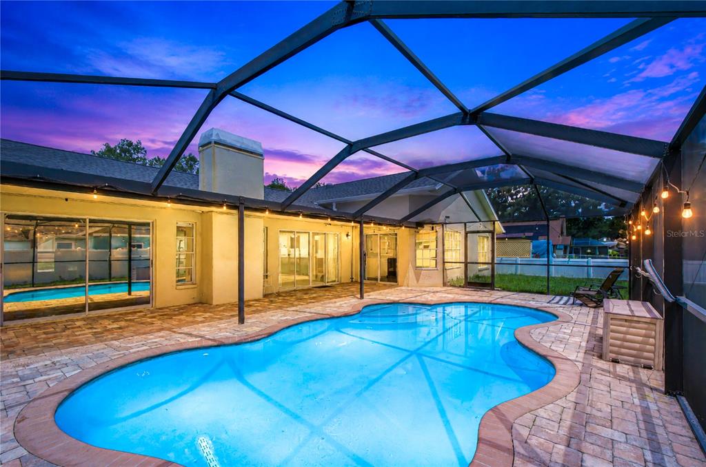 A backyard swimming pool is enclosed by a screened lanai at dusk — 1108 DOCKSIDE DRIVE, LUTZ, FL