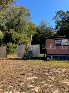 A mobile home exterior sits next to a metal fence in a grassy, wooded lot — 126 YEATTS AVENUE, INTERLACHEN, FL