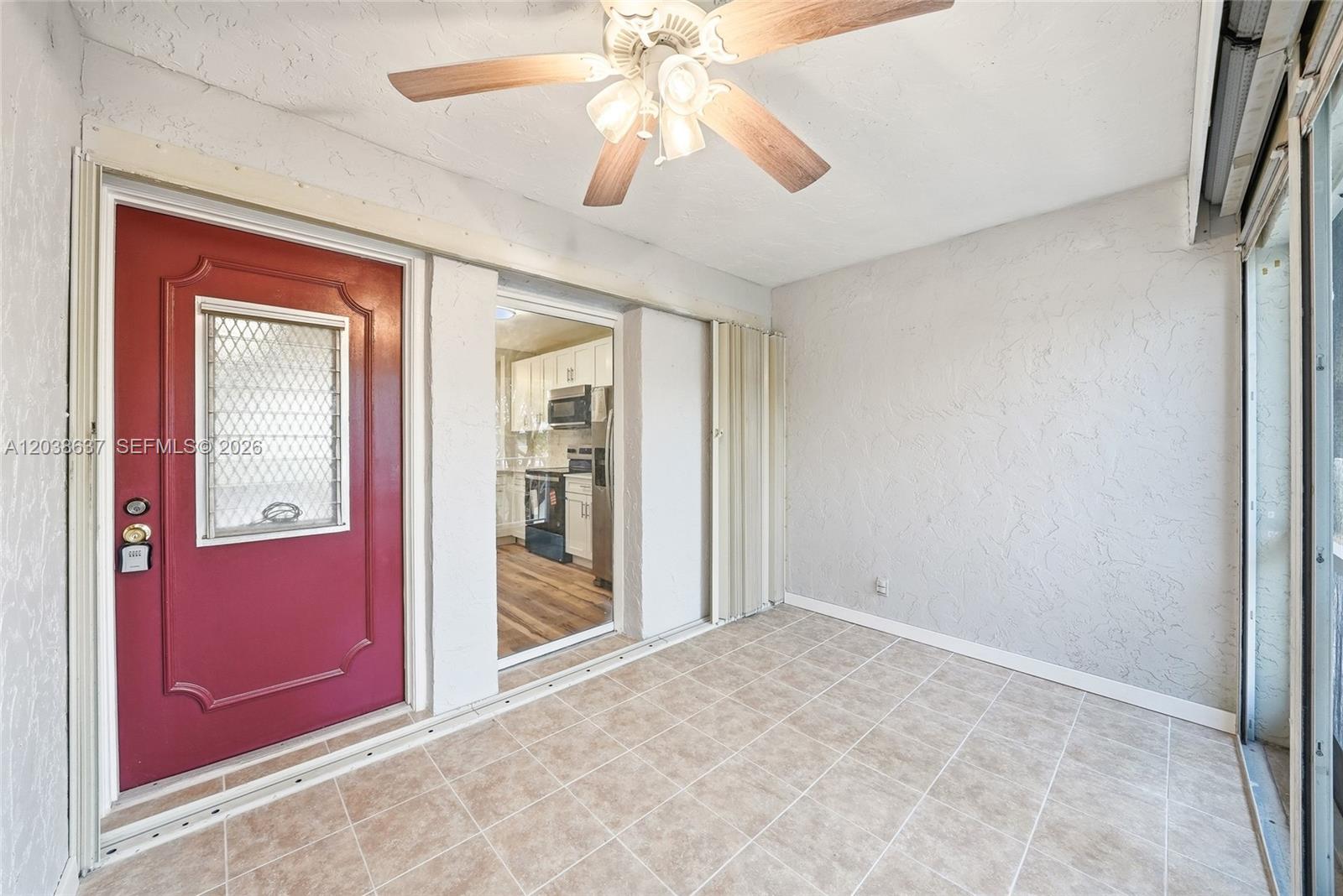 A tiled sunroom features a red door, a ceiling fan, and a view into a kitchen — 860 SE 6 Ave # 311, Deerfield Beach FL 33441, DEERFIELD BEACH, FL