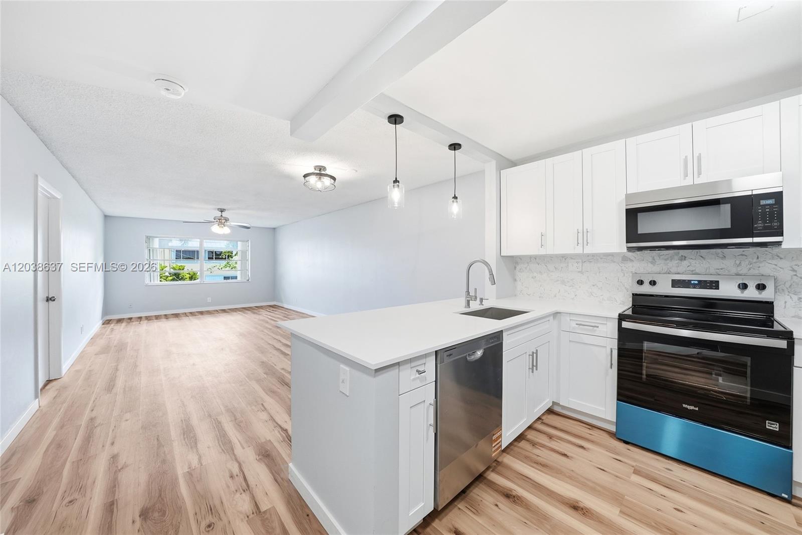 A kitchen with white cabinets and stainless steel appliances opens into a spacious living area — 860 SE 6 Ave # 311, Deerfield Beach FL 33441, DEERFIELD BEACH, FL