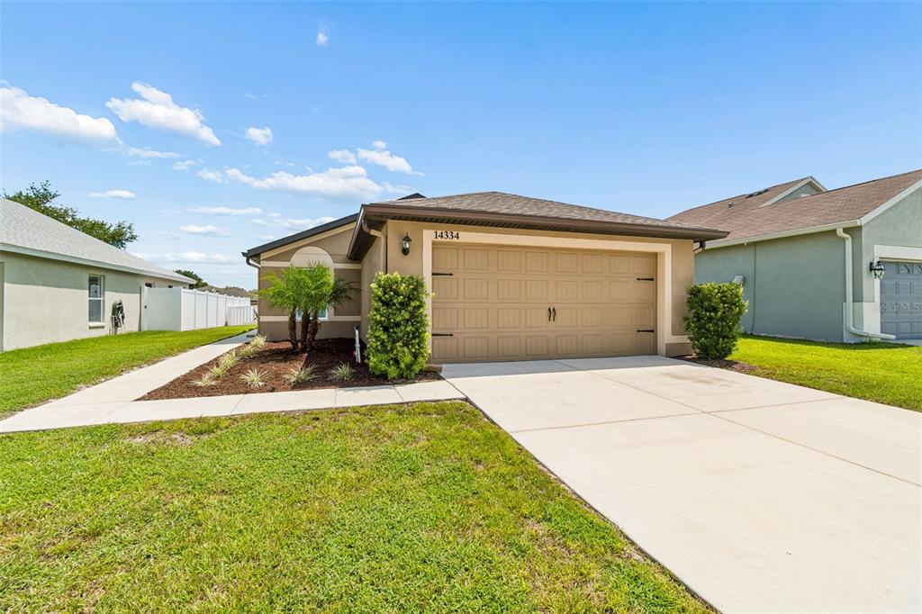 A single-story house with a tan exterior, a two-car garage, and a concrete driveway — 14334 HOLLY HAMMOCK LANE, BROOKSVILLE, FL