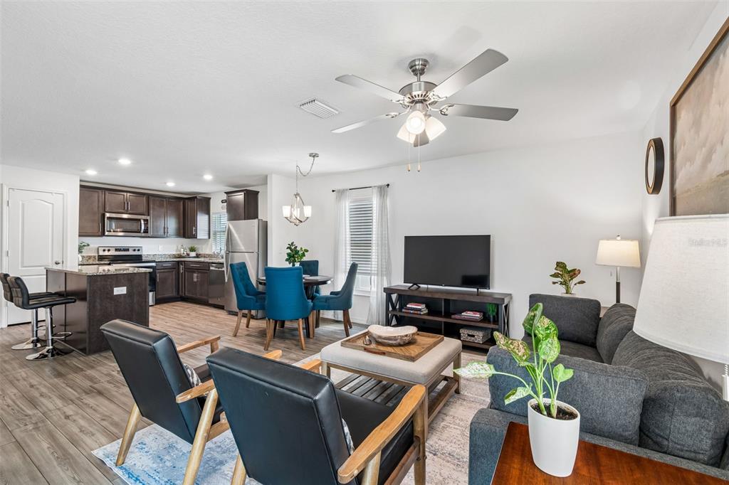 An open-concept living room and kitchen featuring dark cabinetry, blue dining chairs, and gray furniture — 14334 HOLLY HAMMOCK LANE, BROOKSVILLE, FL