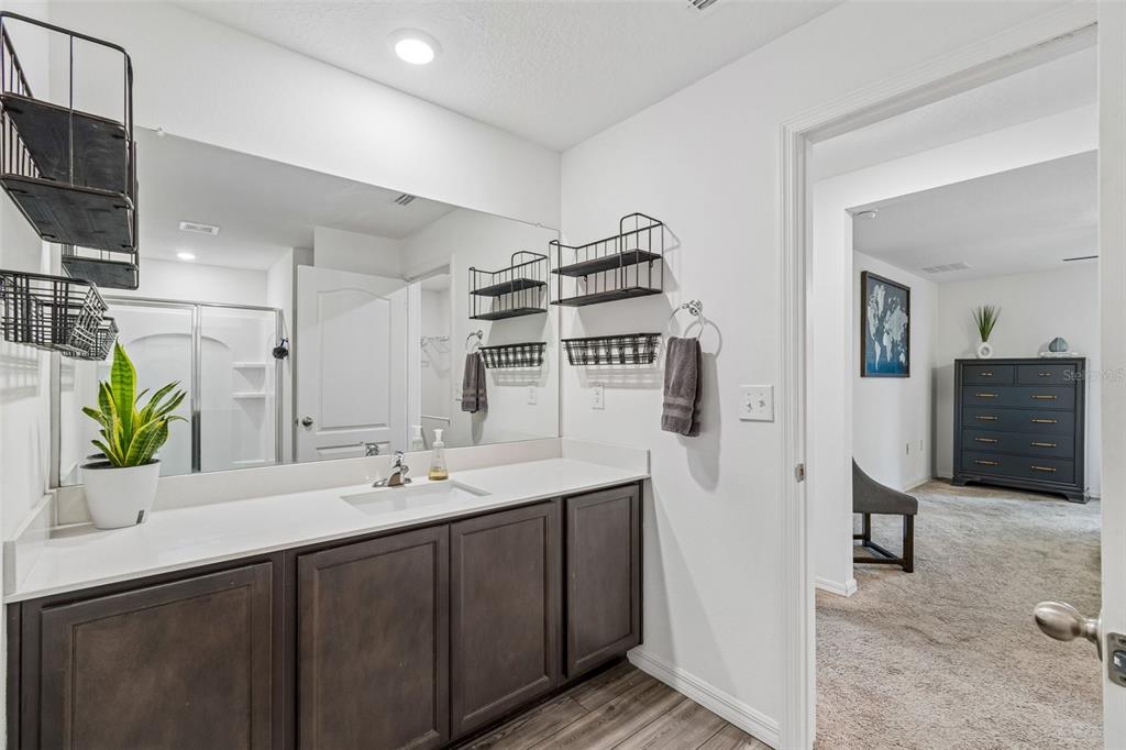 A bathroom with a dark wood vanity, white countertop, and wall-mounted wire storage shelves — 14334 HOLLY HAMMOCK LANE, BROOKSVILLE, FL