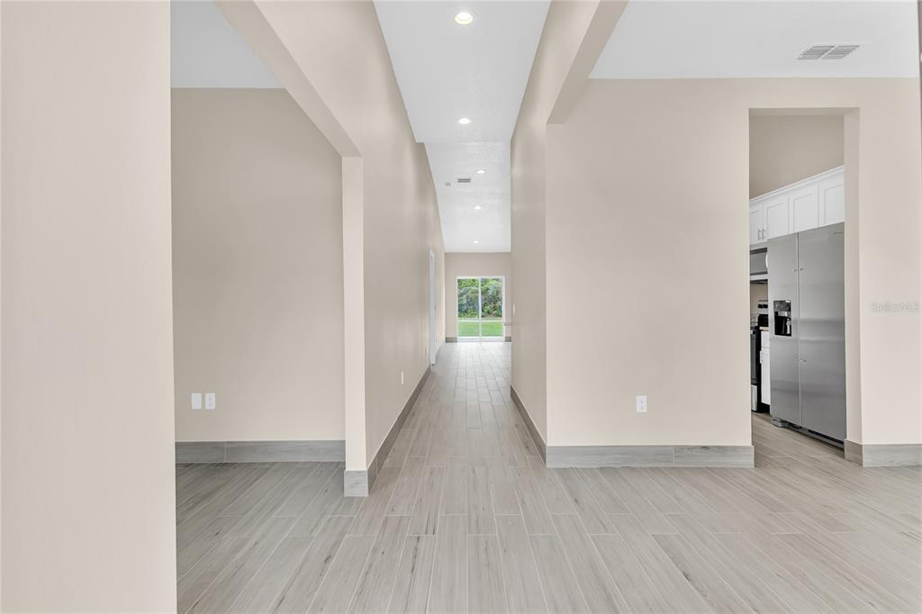 A hallway with light-colored walls and wood-look tile flooring leads toward a windowed exterior view — 17 HERRING COURT, KISSIMMEE, FL
