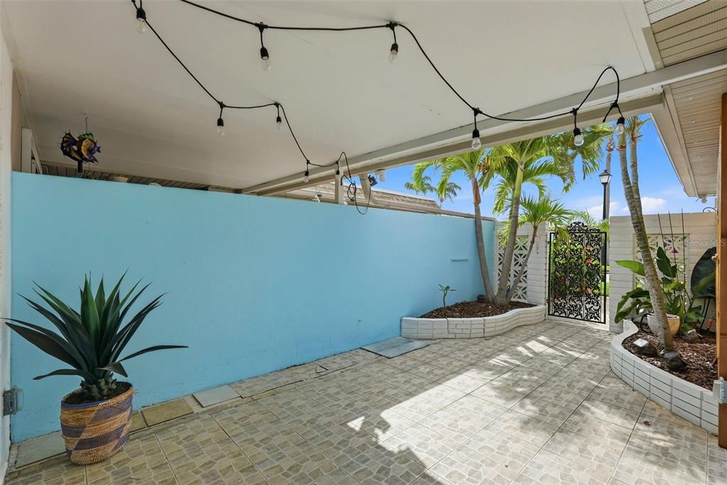 A covered patio features a light blue wall, tiled flooring, string lights, and potted plants — 573 BOCA CIEGA POINT BOULEVARD N, ST PETERSBURG, FL