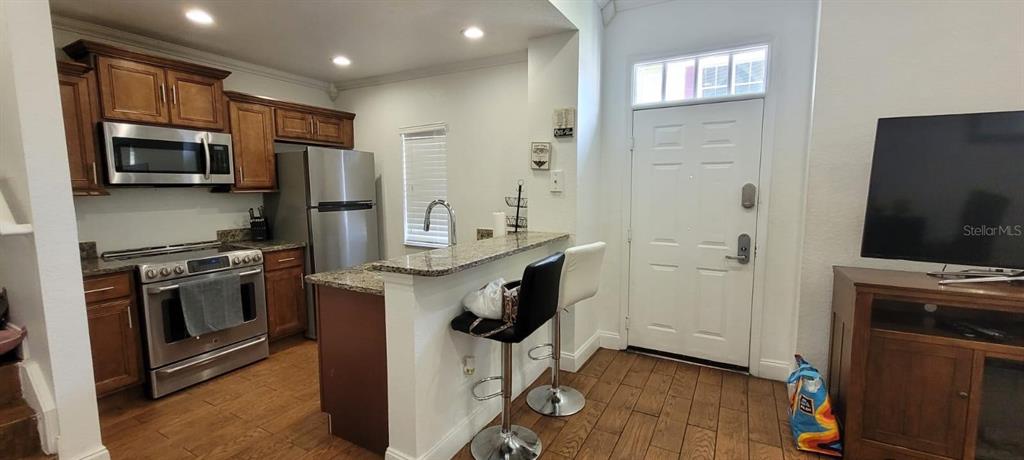 A kitchen with wood cabinets, stainless steel appliances, and a breakfast bar faces an entryway — 4004 SANTA MARIA DRIVE UNIT 101, KISSIMMEE, FL