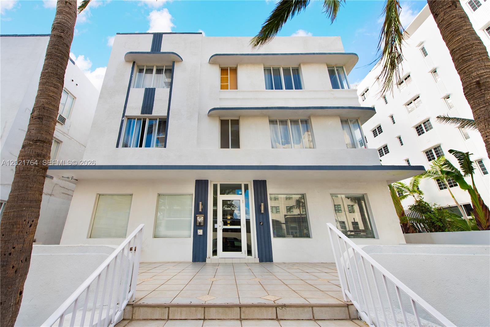 The exterior of a white Art Deco building features blue accents and palm trees — 3710 Collins Ave # 305, Miami Beach FL 33140, MIAMI BEACH, FL