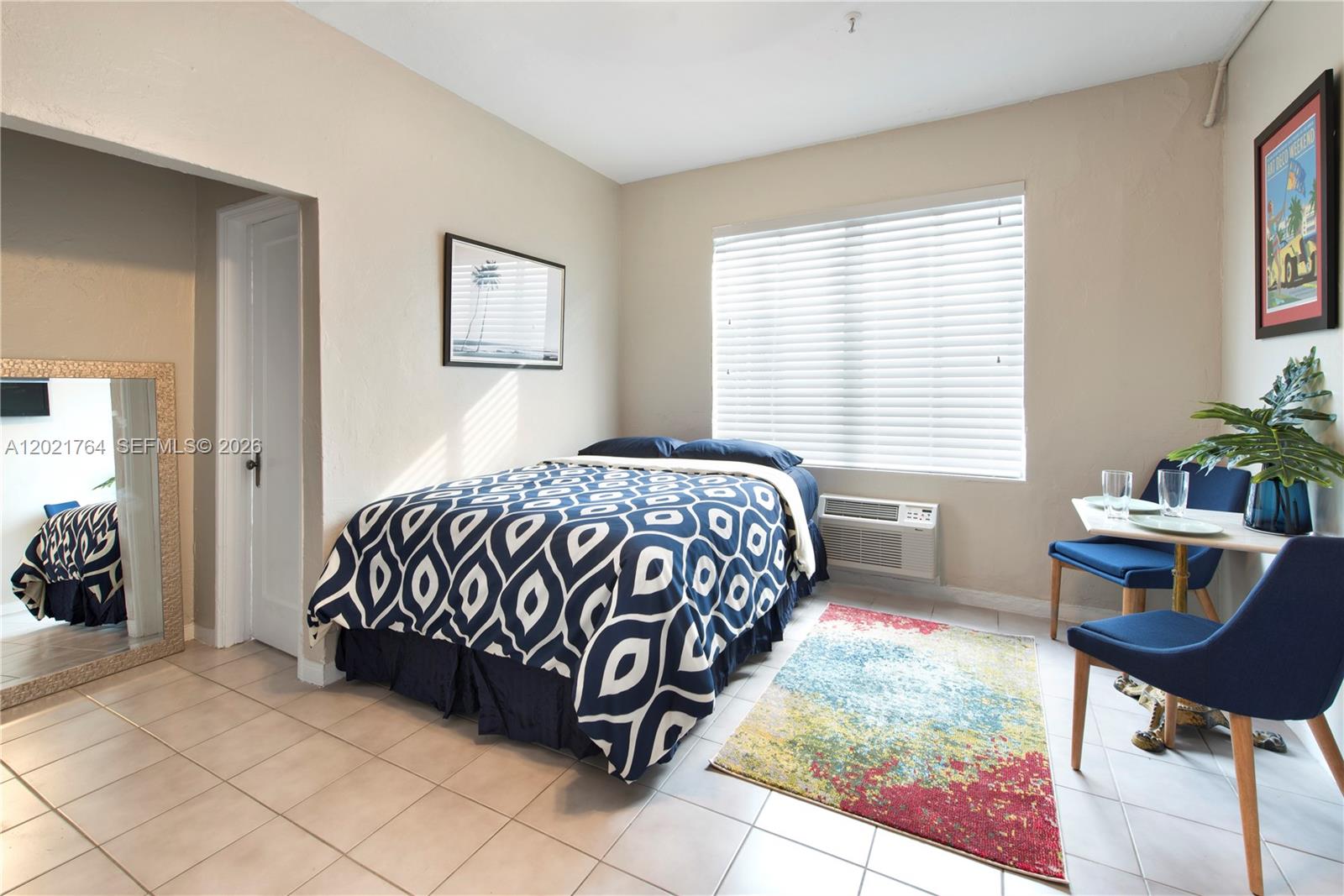 A bedroom features a patterned bedspread, a small dining set, and a large floor mirror — 3710 Collins Ave # 305, Miami Beach FL 33140, MIAMI BEACH, FL
