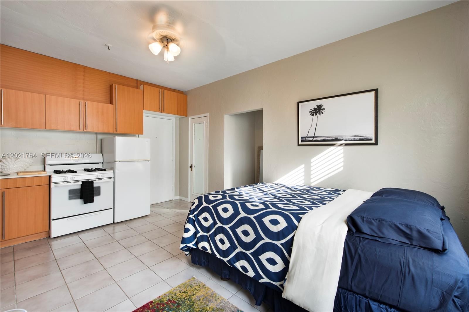 A studio apartment features a kitchenette with wooden cabinets, a white stove, and a bed — 3710 Collins Ave # 305, Miami Beach FL 33140, MIAMI BEACH, FL