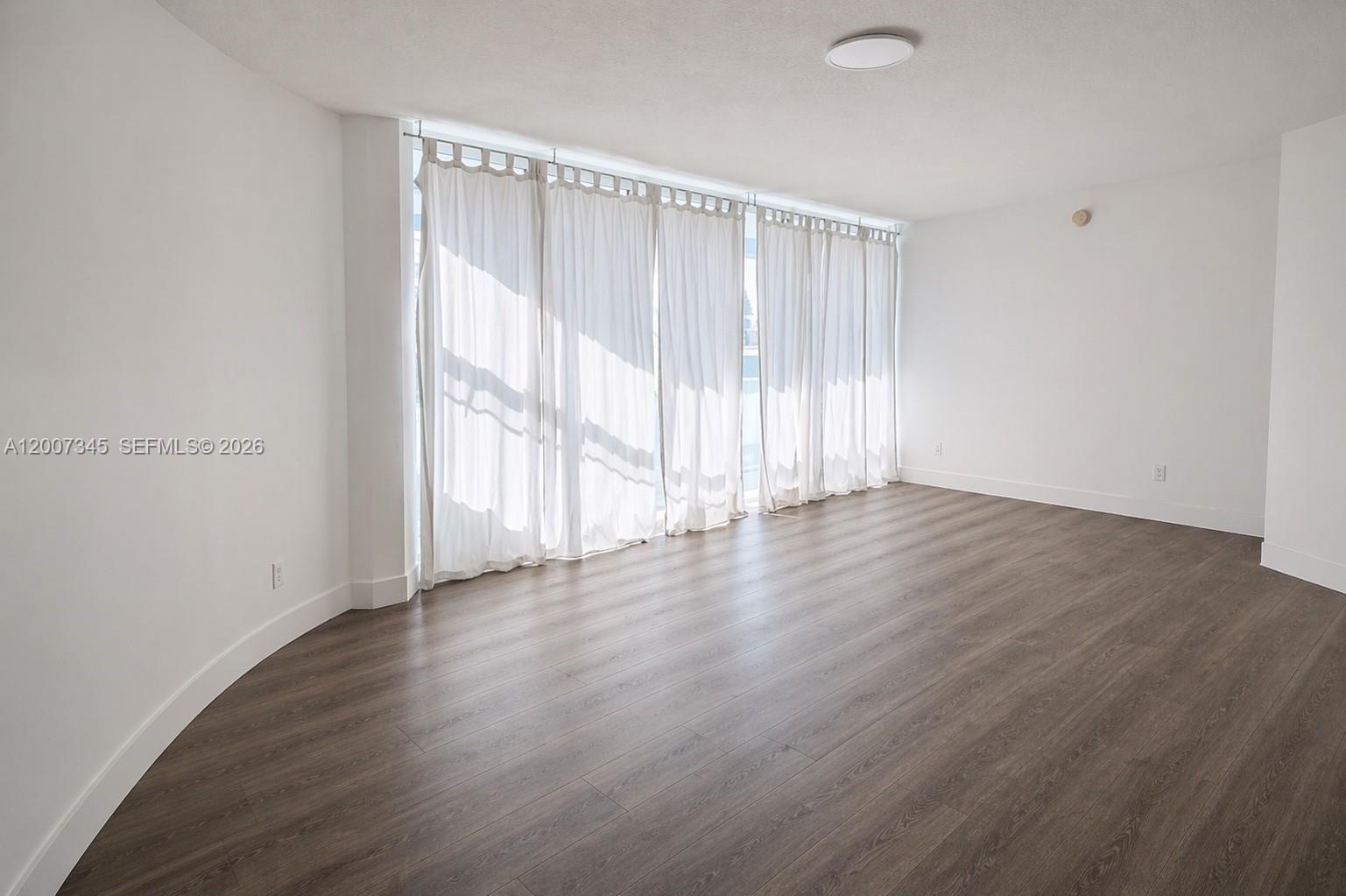 An empty room features white walls, dark wood-look flooring, and floor-to-ceiling curtains — 6580 INDIAN CREEK DR # 511, Miami Beach FL 33141, MIAMI BEACH, FL
