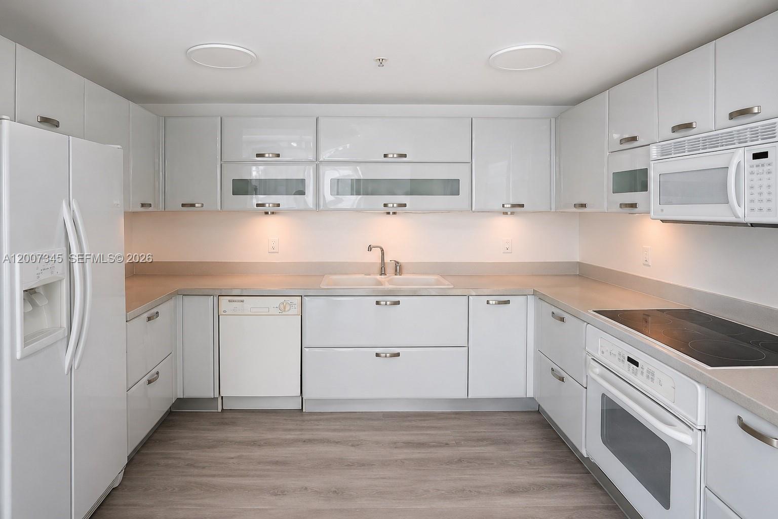 A modern kitchen features white glossy cabinets, stainless steel appliances, and light-colored countertops — 6580 INDIAN CREEK DR # 511, Miami Beach FL 33141, MIAMI BEACH, FL