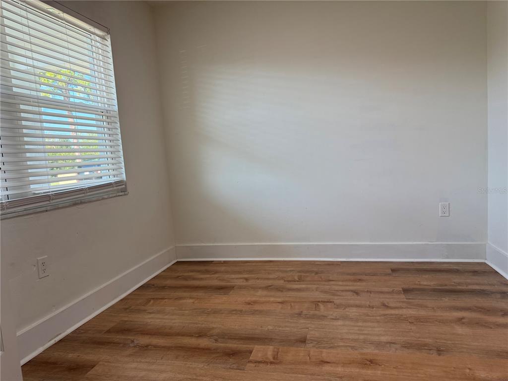 An empty room features light-colored walls, wood-look flooring, white baseboards, and a window with blinds — 1001 77TH AVENUE N UNIT 102, ST PETERSBURG, FL